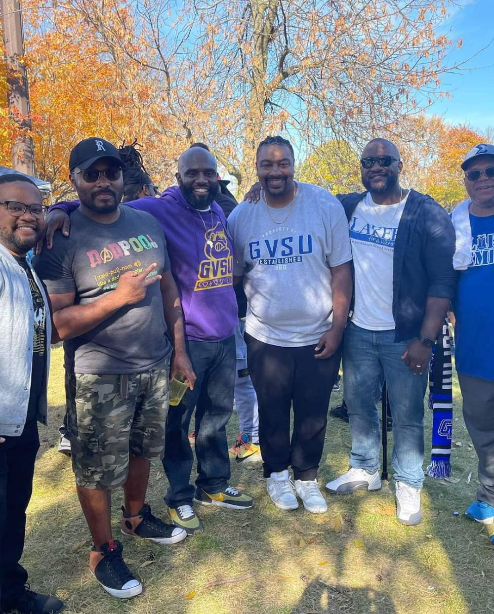 A group of alumni pose for a photo at the tailgate in GVSU gear.